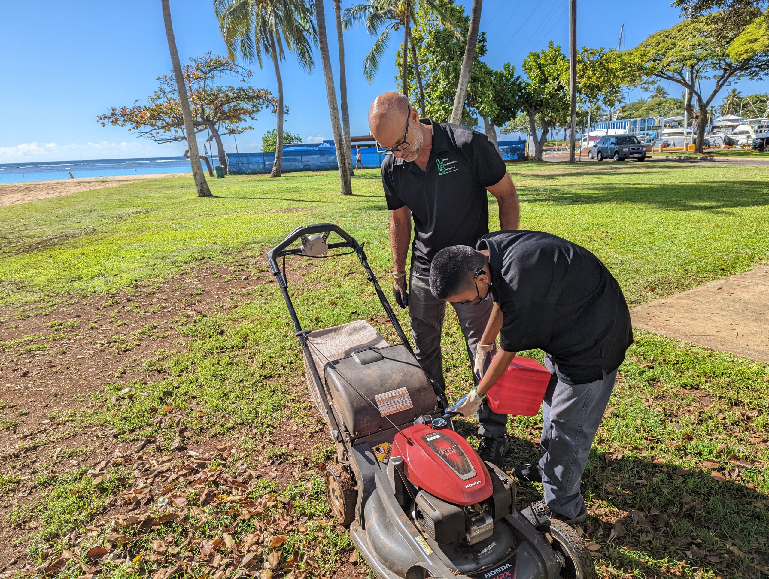 A male filling up a Lawn Mower outdoors.